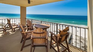 Ein Balkon mit Holzstühlen und einem Tisch, der auf einen Strand mit klarem, blauem Wasser und sandigem Ufer blickt.