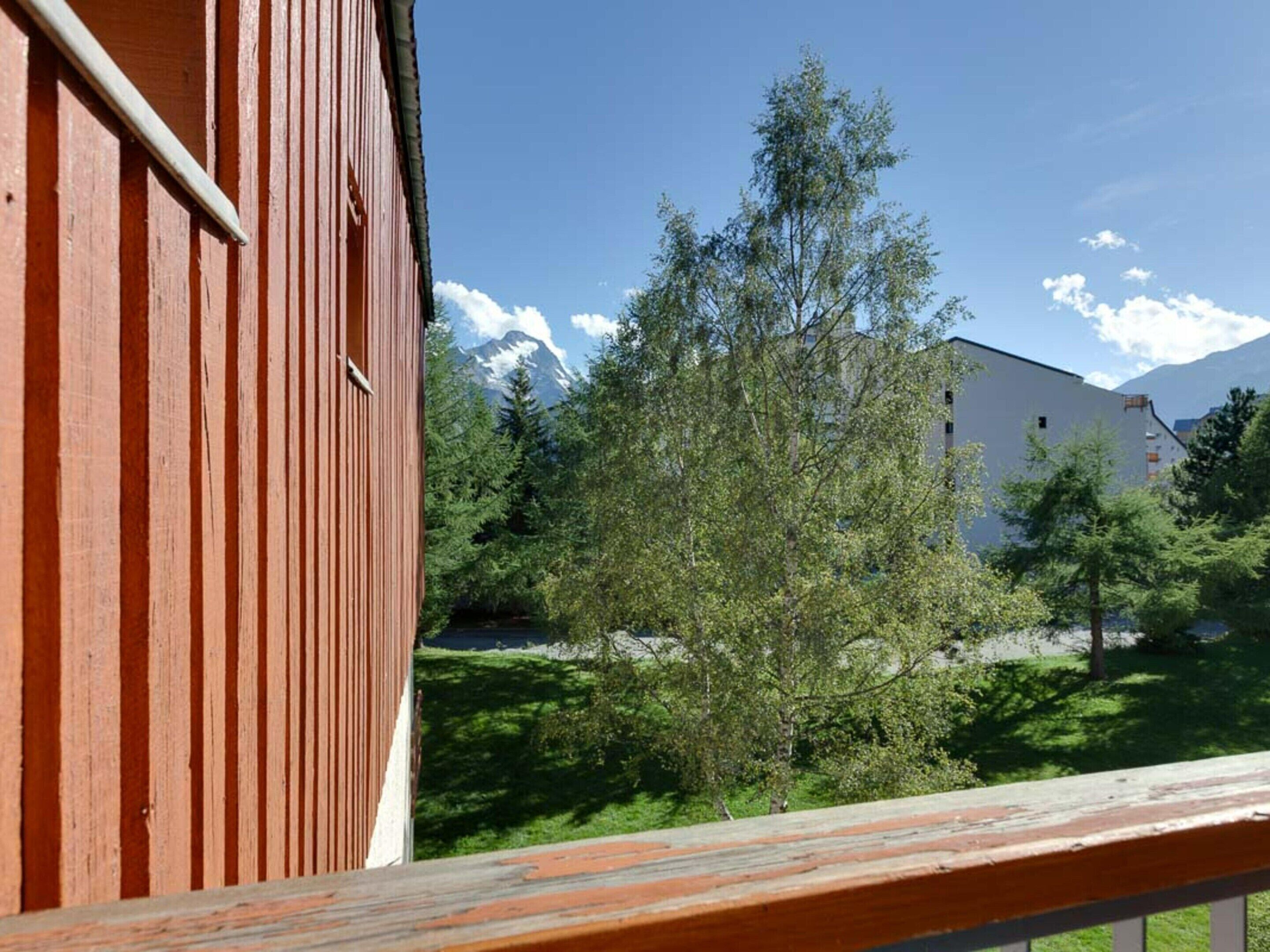Un balcón de madera con vistas a un edificio y árboles.