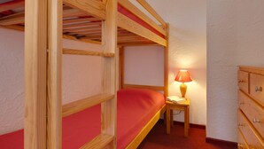 Une chambre avec un lit superposé, une commode en bois et une petite table avec une lampe.