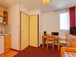 Ein kompakter Raum mit Küchenzeile, einem Essbereich mit Tisch und Stühlen, einem Bett und einem Fenster mit Vorhängen.