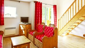 Een kamer met een houten trap, een televisie, een bureau en een zithoek.