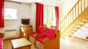 A room with a wooden staircase, a TV, a desk, and a sofa set.