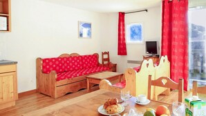 Een gezellige kamer met een houten bank, een eettafel met ontbijtartikelen, een televisie en een raam met gordijnen.