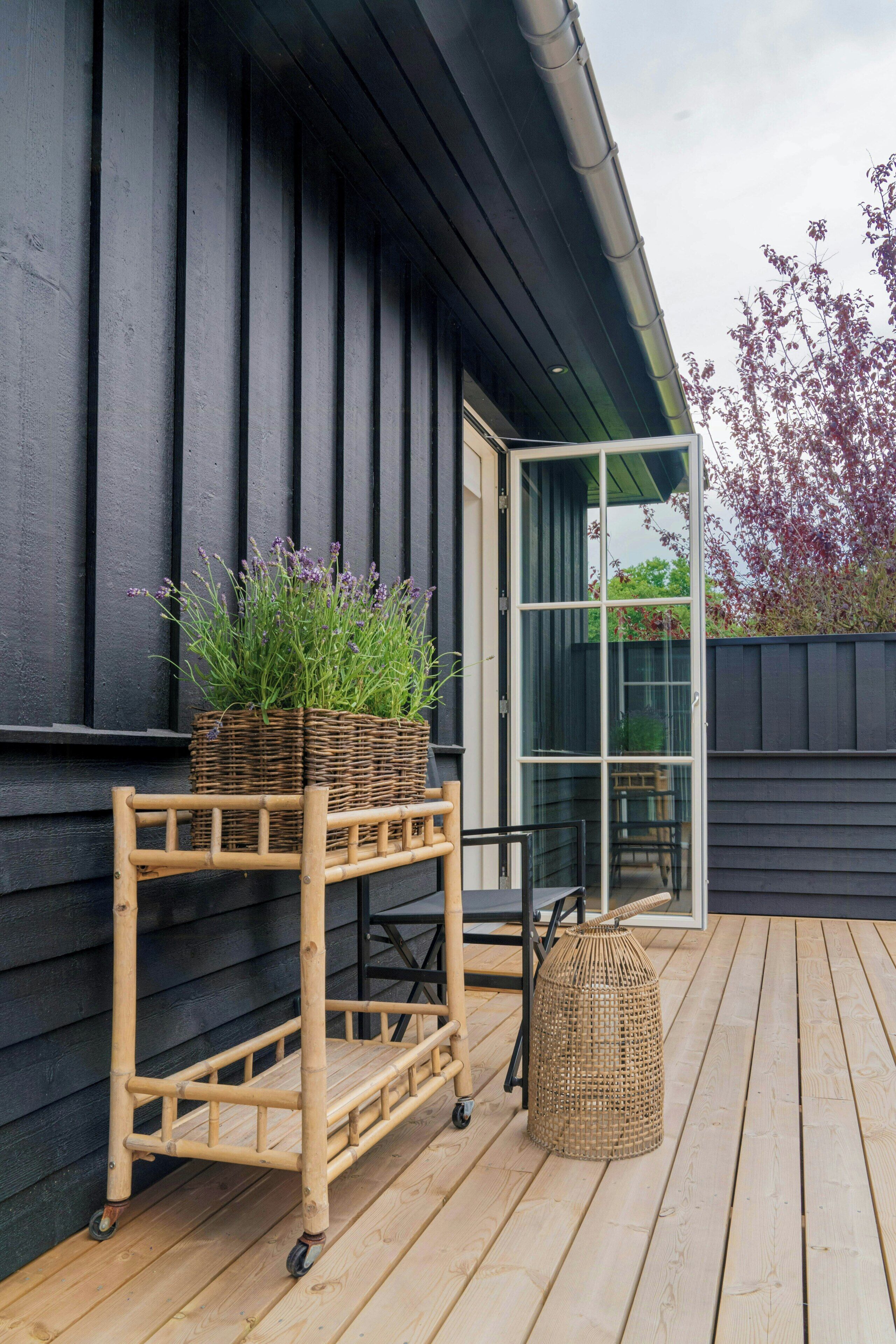 A wooden outdoor deck with a wicker cart holding plants, a wicker basket, and a wicker lamp.