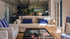 Een moderne woonkamer met een witte bank, gestreepte kussens, een salontafel met glazen en uitzicht op het buitengebied.