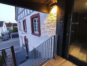 Un edificio con fachada blanca y marcos de ventana rojos, una escalera metálica y un ascensor.