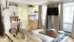 A modern kitchen with white cabinets, a microwave, and a coffee maker. There is a dining area with a wooden table and a sofa with cushions. - NOX Hotel (Walzbachtal)