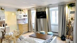 A modern living room with a sofa, a coffee table, a TV, and a kitchen area with a microwave. - NOX Hotel (Walzbachtal)