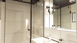 A modern bathroom with a large mirror, a white sink, and a glass shower enclosure. - NOX Hotel (Walzbachtal)