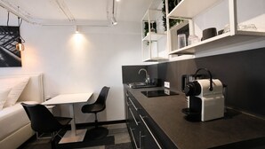 Una cocina moderna con encimera negra, armarios blancos, una cafetera y una zona de comedor con mesa blanca y sillas negras.