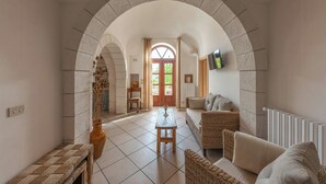 An interior with an arched doorway, a tiled floor, a wooden table, a sofa, and a television mounted on the wall. - Traditional trullo with pool (Ostuni)