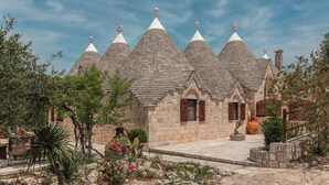 A stone building with multiple conical roofs and a courtyard with plants and a large vase. - Traditional trullo with pool (Ostuni)