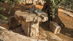 A stone table with a book and a coffee pot, surrounded by rocks and olive trees. - Traditional trullo with pool (Ostuni)
