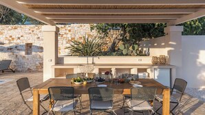 An outdoor dining area with a stone wall, a wooden pergola, and a table set for six. - Traditional trullo with pool (Ostuni)