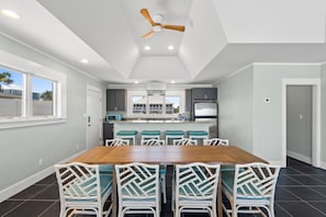 Une cuisine moderne dotée d’un îlot central, de meubles blancs et d’un coin repas avec une table en bois et des chaises blanches.