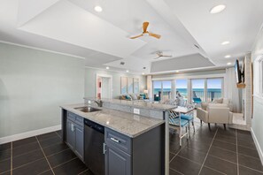 A modern kitchen with granite countertops, a dishwasher, and a dining area with a view of the ocean.