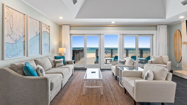 A spacious living room with a large glass door leading to a balcony with a view of the beach. There are two sofas, a coffee table, and a TV. - Beachfront Breeze: Beachfront, Close to town center, Pet friendly, direct beach (St. George Island)