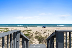 Une plage avec une promenade en bois menant à un parasol bleu.