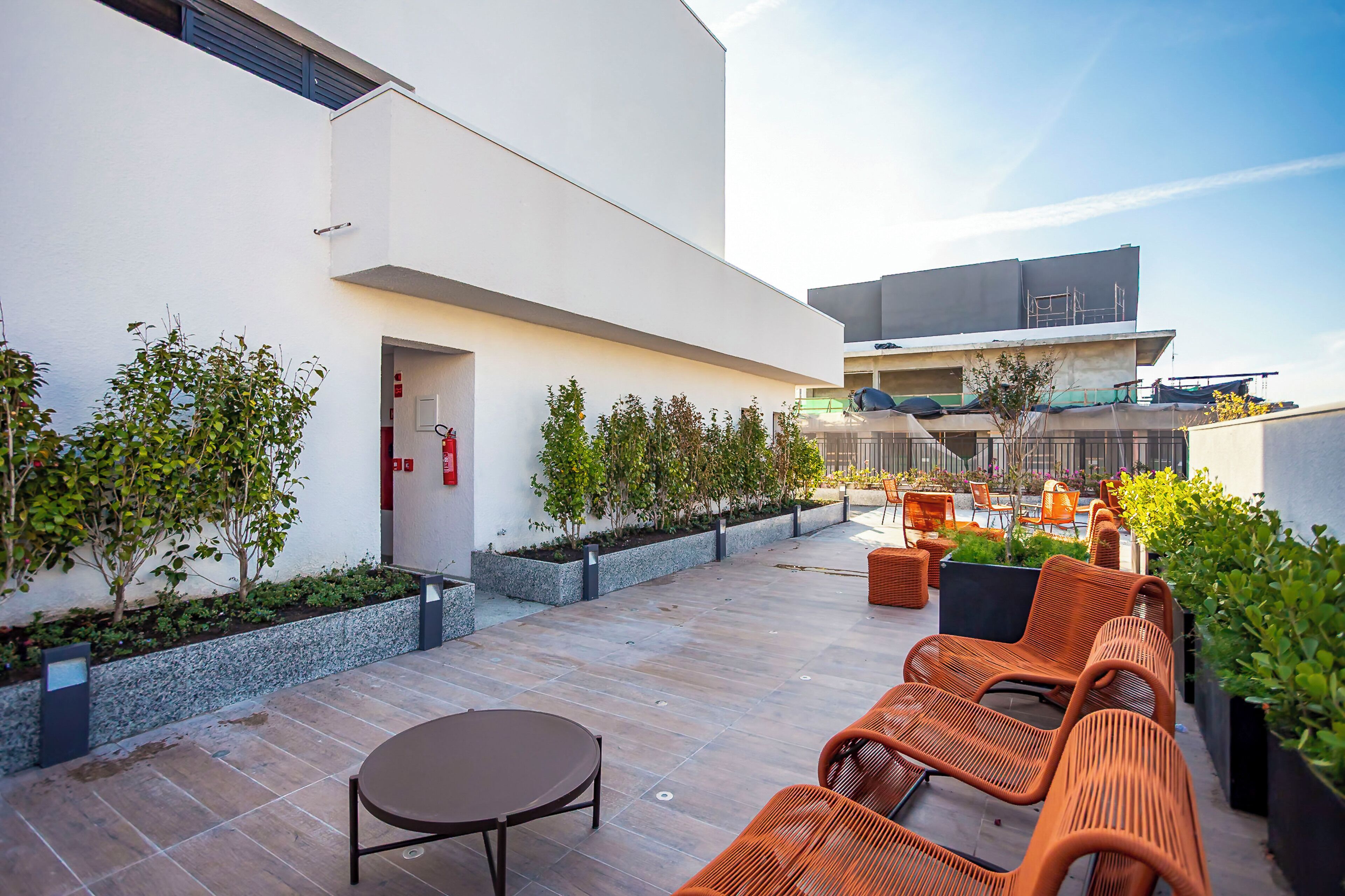 Un patio moderno al aire libre con mobiliario de mimbre, una mesa redonda y plantas en macetas.