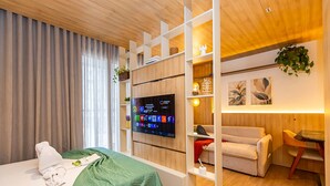 Una habitación de hotel con cama, televisión, sofá, una mesita y una planta.