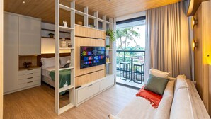 Una habitación moderna con televisor, sofá, cama, balcón con mesa y armario corredero.