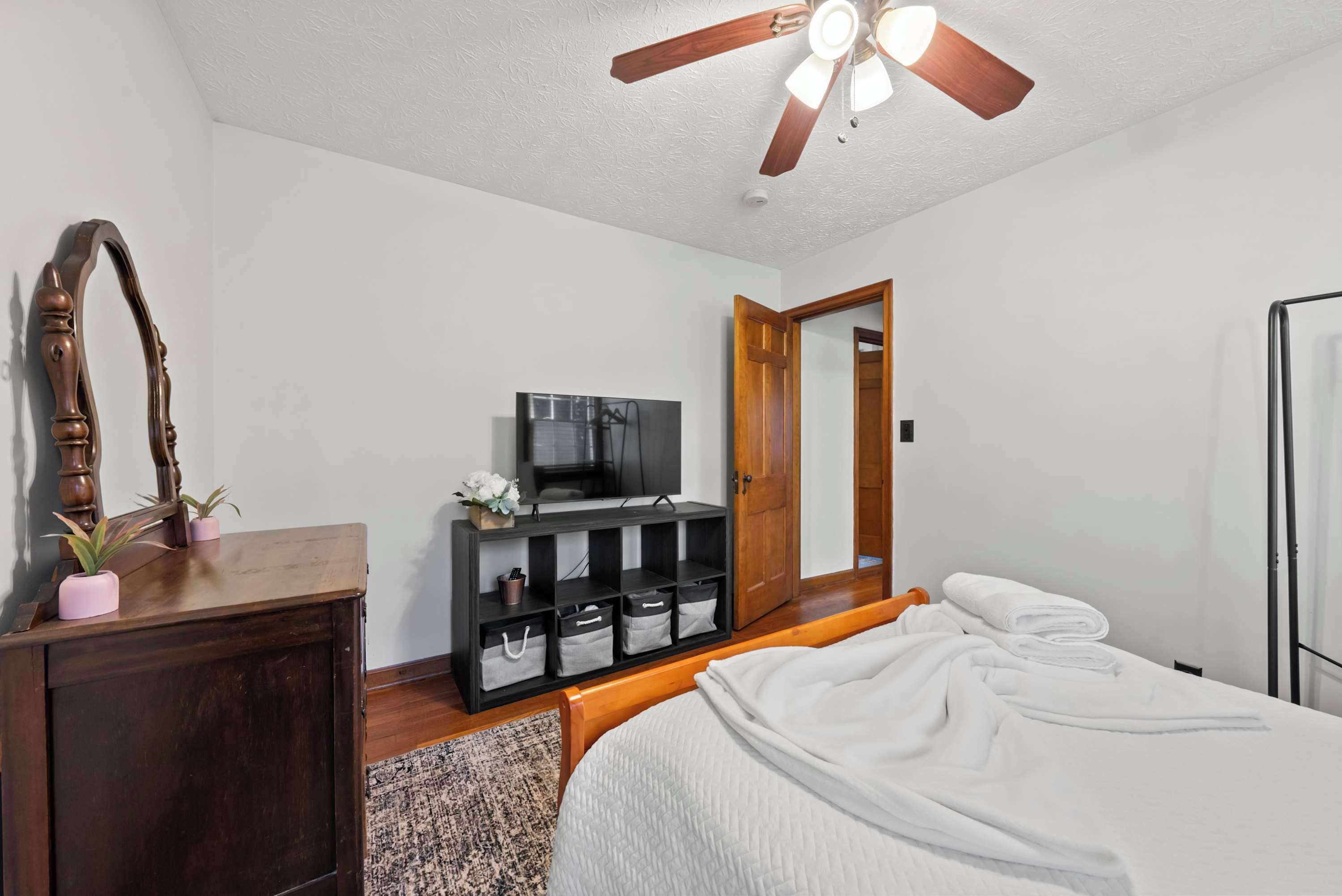 A bedroom with a bed, a wooden dresser, a television, and a ceiling fan.