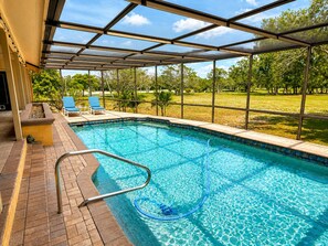A swimming pool with a glass enclosure, a brick deck, and a view of a grassy area with trees. - Renovated 3/3.5 Pool home, Private Beach Access (Longboat Key)