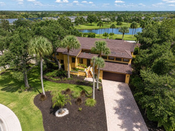 A two-story house with a paved driveway, surrounded by lush greenery and a lake view. - Renovated 3/3.5 Pool home, Private Beach Access (Longboat Key)