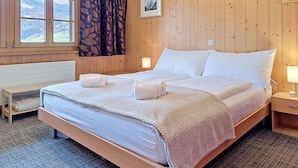 Een kamer met houten lambrisering, een bed, een bank, een raam met gordijnen en een ingelijst kunstwerk aan de muur.