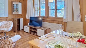 Een kamer met houten lambrisering, een televisie, een eettafel, stoelen en een rieten mand.