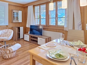 Ein Zimmer mit Holzwänden, einem Fernseher, einem Esstisch, Stühlen und einem Korbwäschesystem.