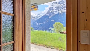 Een houten deur die leidt naar een kamer met uitzicht op een bergachtig landschap.