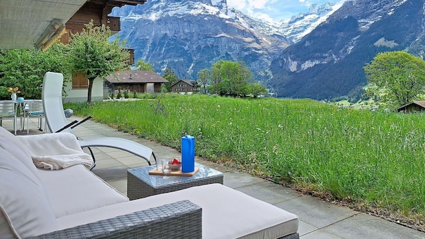 Een terras met buitenmeubilair, uitzicht op besneeuwde bergen en een gazon.