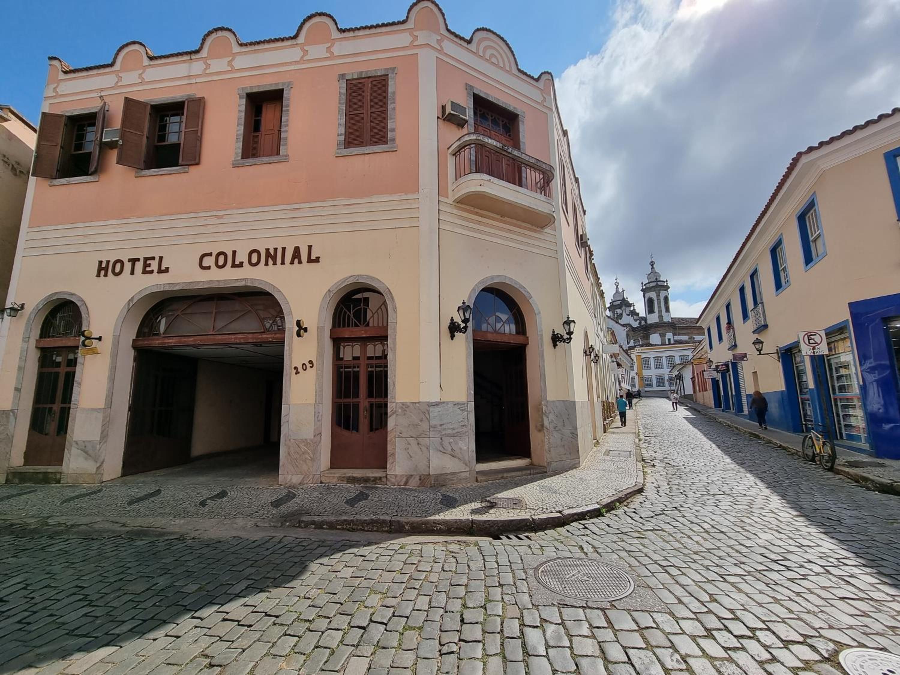 Um edifício histórico com a placa 'HOTEL COLONIAL' e uma rua de paralelepípedos.