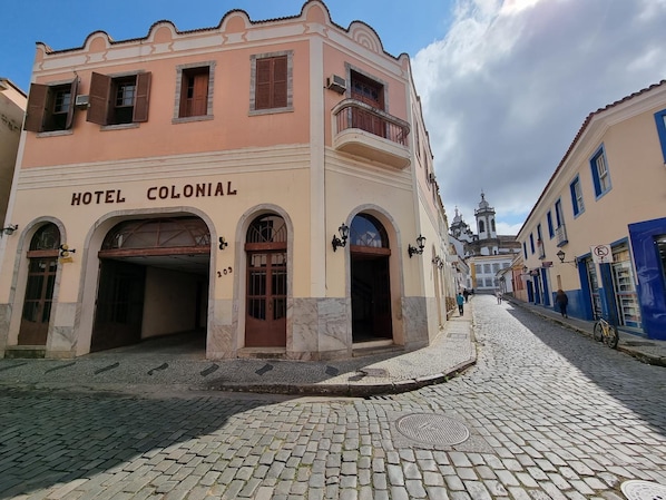 Un bâtiment historique portant l’enseigne « HÔTEL COLONIAL » et une rue pavée.