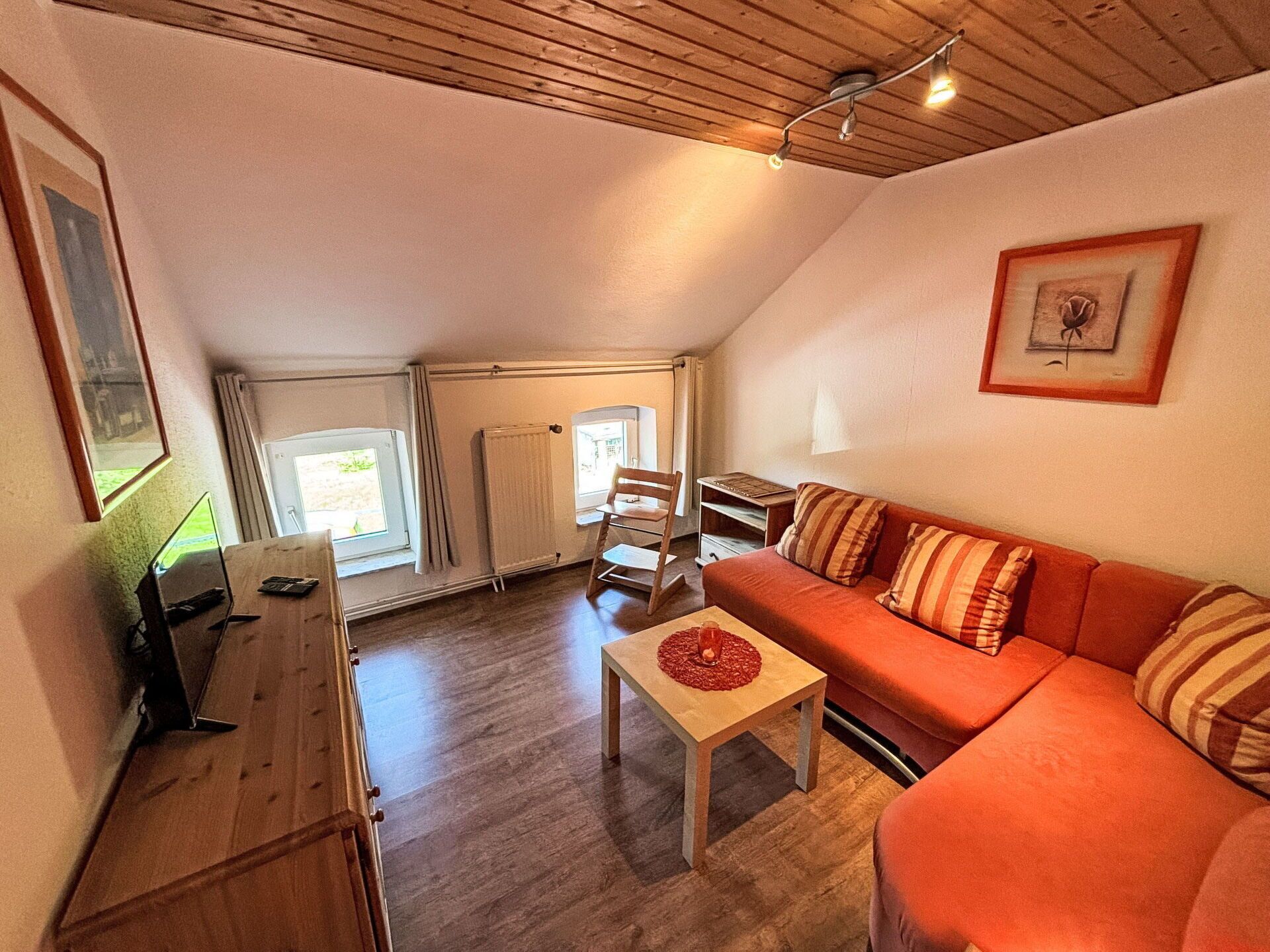 Un salon chaleureux avec un plafond en bois, un canapé rouge, une petite table et un fauteuil.