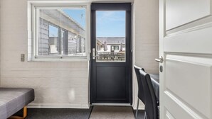 A room with a black door, a window with blinds, a small table, and a chair. - 40 Person Holiday Home in Skaerbaek (Skaerbaek)