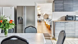 A modern kitchen with a built-in microwave, a refrigerator, and a dining area with a table and chairs. - 40 Person Holiday Home in Skaerbaek (Skaerbaek)
