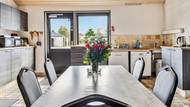 A dining area with a table, chairs, a vase with flowers, and a view through a window. - 40 Person Holiday Home in Skaerbaek (Skaerbaek)