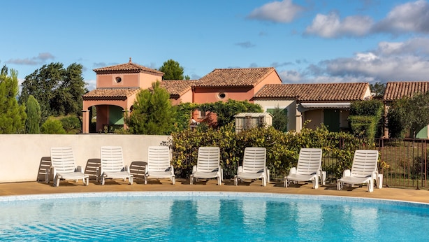 A swimming pool with lounge chairs, a building with a tiled roof, and greenery in the background. - Home for 4 With Private Parking (Homps)