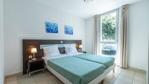 A double bed with a green bedspread, two bedside tables with lamps, a large window with curtains, and two wall-mounted paintings. - Spacious French Riviera Stay for 6 (Cagnes-sur-Mer)