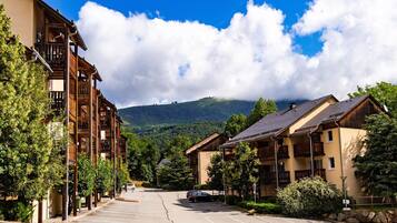A parking lot with buildings on either side, a clear sky, and a mountain in the background.