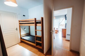 Ein Zimmer mit einem Etagenbett, einer Tür und Blick in einen anderen Raum mit einer Küchenzeile.