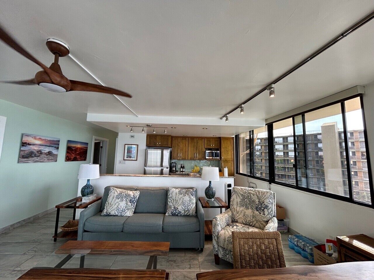 Ein modernes Wohnzimmer mit Sofa, Sessel und Couchtisch, im Hintergrund eine Küche und große Fenster mit Blick auf die Stadt.