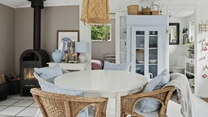 Ein gemütliches Zimmer mit Kamin, Korbmöbeln und einem weißen Esstisch.
