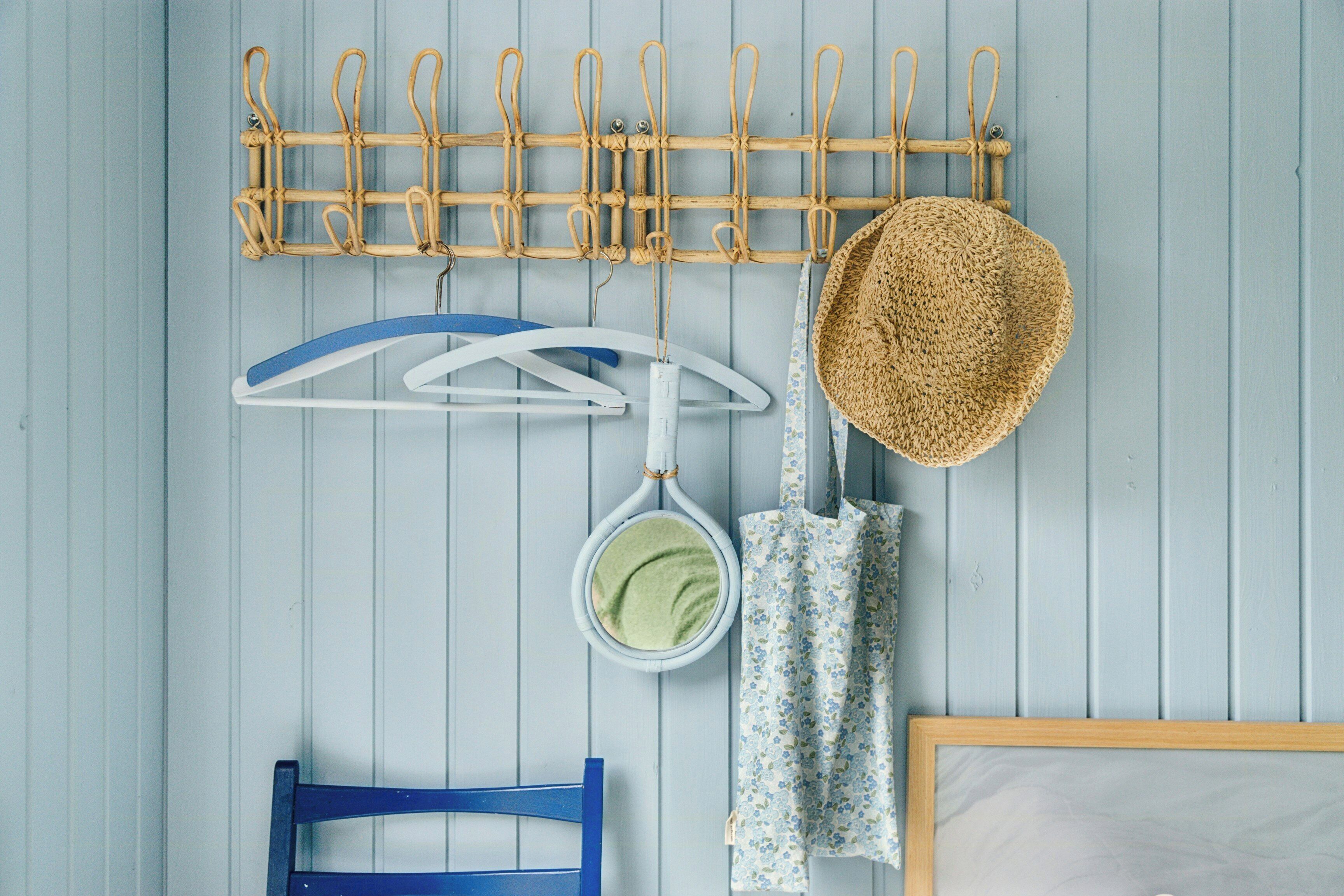 Quarto com uma cadeira azul, um cabideiro de madeira, um chapéu, um guarda-chuva branco, um pendurar azul e um quadro numa parede de madeira azul clara.
