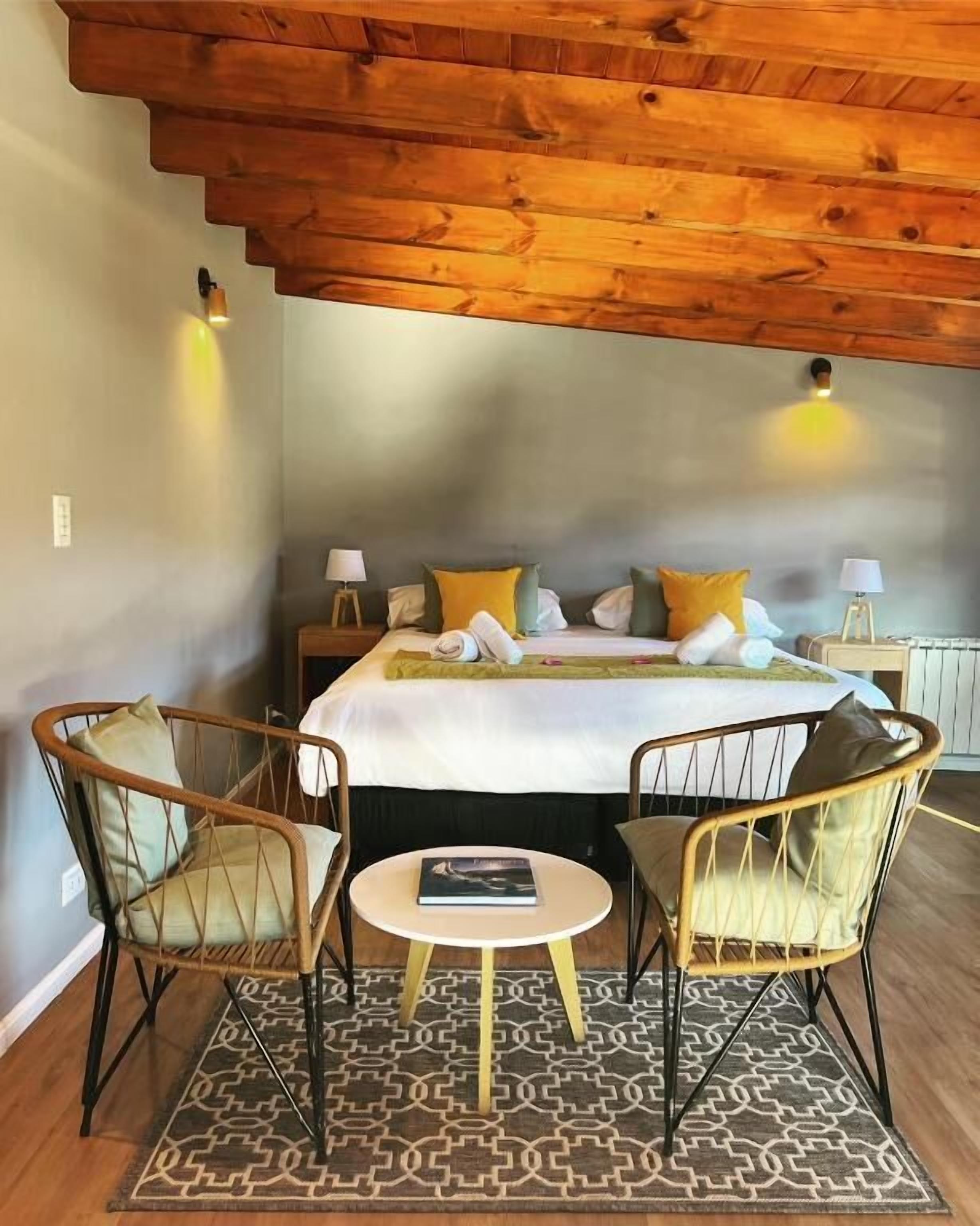 Ein Schlafzimmer mit einem Bett, zwei Stühlen, einem kleinen Tisch und einem gemusterten Teppich.