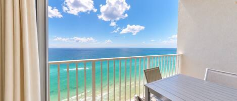 A balcony with a view of the ocean and a table with chairs.