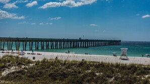 Eine Pier, die sich ins Meer erstreckt, mit Liegestühlen und Sonnenschirmen am Strand.