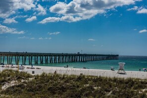 Eine Pier, die sich ins Meer erstreckt, mit Liegestühlen und Sonnenschirmen am Strand.